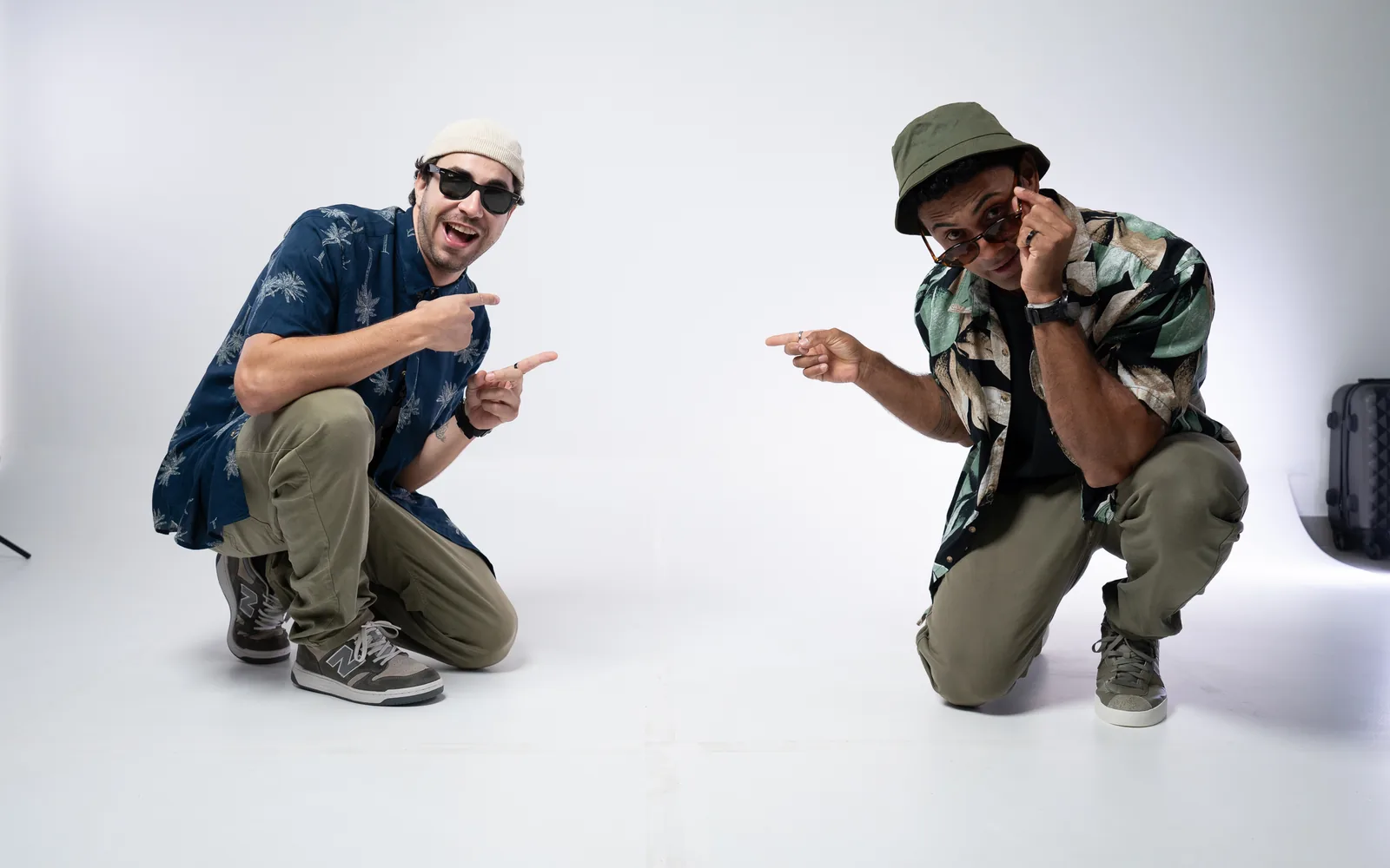 Dudu e Yves agachados, apontando um para o outro